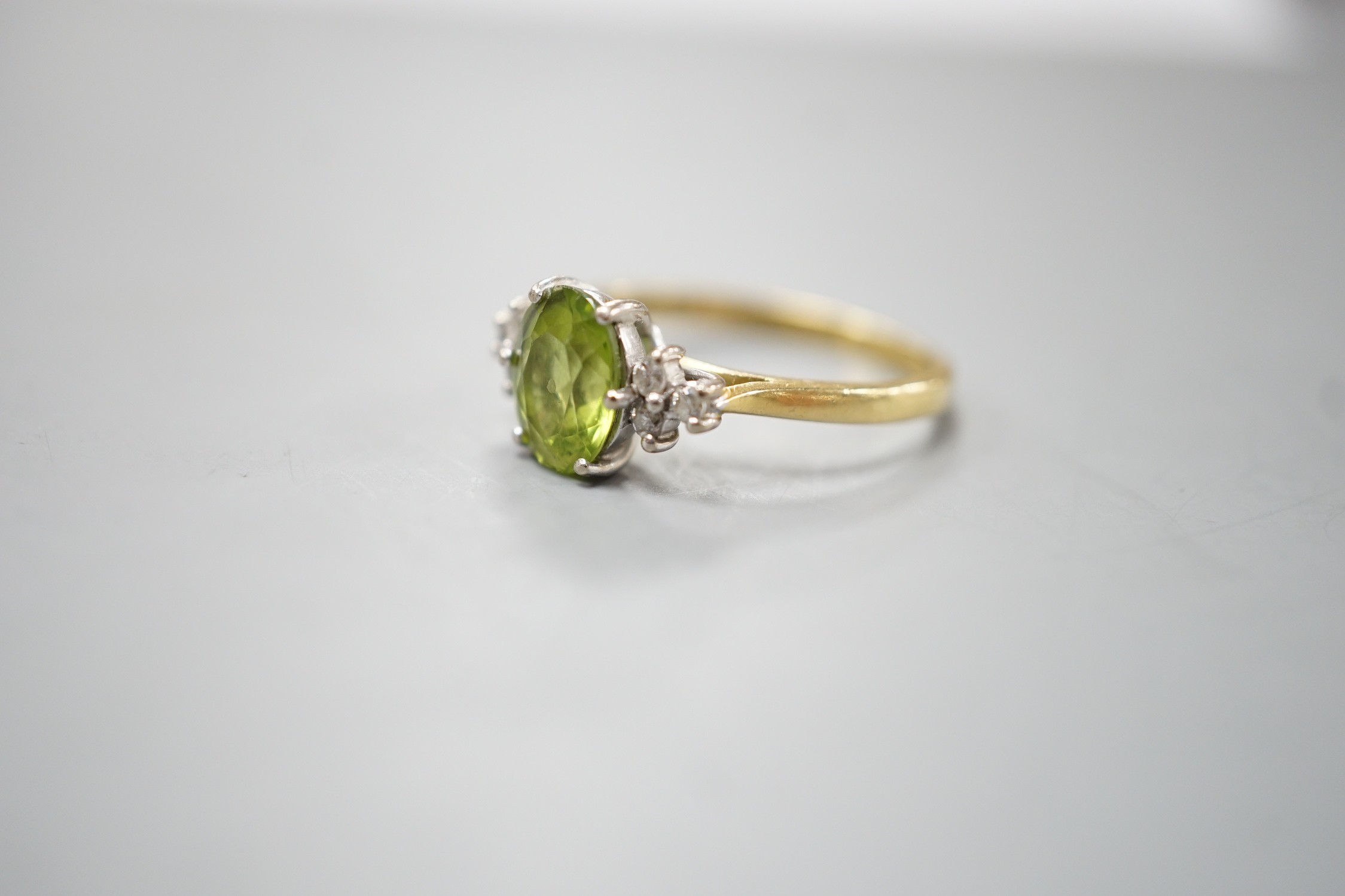 A modern 18ct gold and oval cut peridot ring, with diamond set shoulders, size M, gross weight 3 grams.